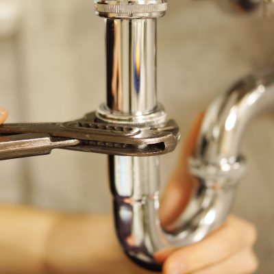 Plumbing repair service. Professional installer with spanner checking pipe.